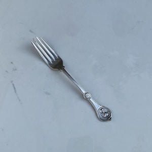 May include: A silver fork with a decorative handle featuring a floral design. The handle is ornate and has a detailed design.