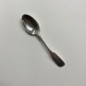 May include: A silver teaspoon with a rounded bowl and a simple, elegant design. The handle is engraved with the text "C. Hunt."