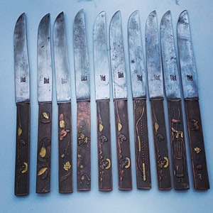 K&ouml;nnte beinhalten: Zehn dekorative Messer mit verzierten Griffen. Die Messer zeigen eine Vielzahl von Designs, darunter florale, geometrische und abstrakte Muster. Die Klingen sind alle aus Metall und haben eine polierte Oberfl&auml;che.