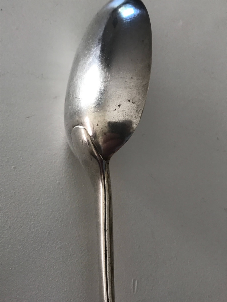 Może przedstawiać: Zbliżenie srebrnej łyżki. Łyżka ma zaokrągloną miseczkę i długi, smukły trzonek. Łyżka jest wykonana z błyszczącego, odblaskowego metalu, a powierzchnia wykazuje niewielkie zużycie. Łyżka jest prawdopodobnie do jedzenia.