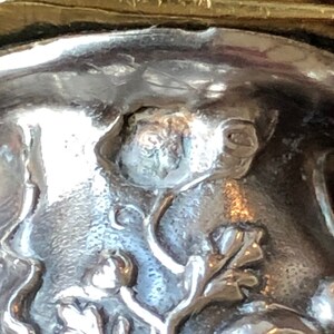 May include: Close-up of a silver bottle stopper with a detailed floral design. The stopper features a small, raised butterfly in the center.