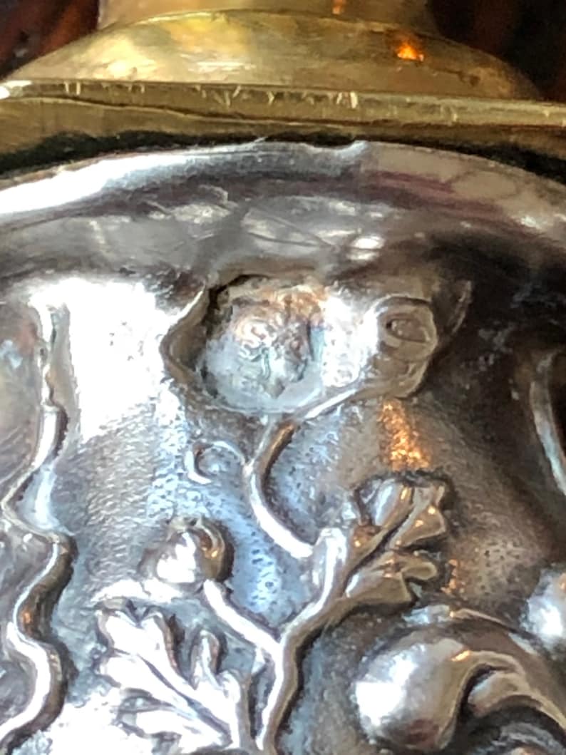 May include: Close-up of a silver bottle stopper with a detailed floral design. The stopper features a small, raised butterfly in the center.