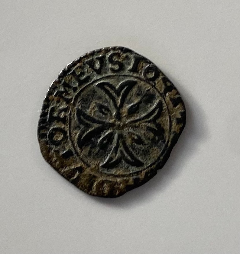 May include: A close-up of a silver coin with a cross design and the inscription "REX" around the edge.