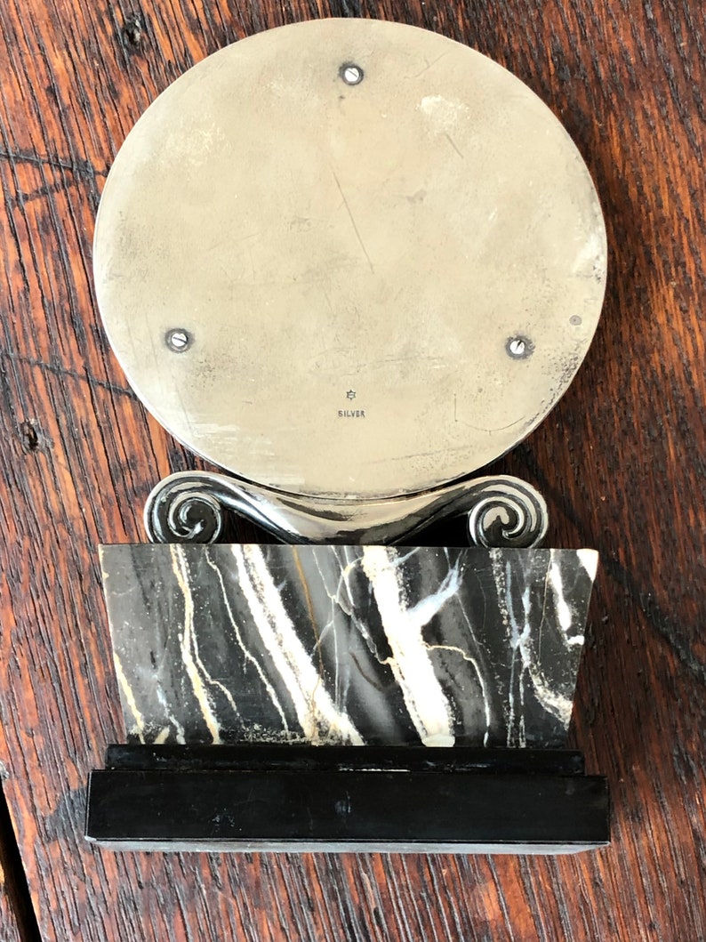 May include: A silver circular mirror with a black and white marble base and a black wooden base. The mirror has a silver inscription that reads "925 SILVER".