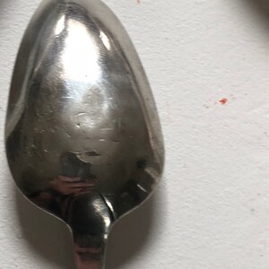 Puede incluir: Una cuchara de plata con un cuenco redondeado de forma ovalada. La cuchara est&aacute; pulida y refleja la luz.