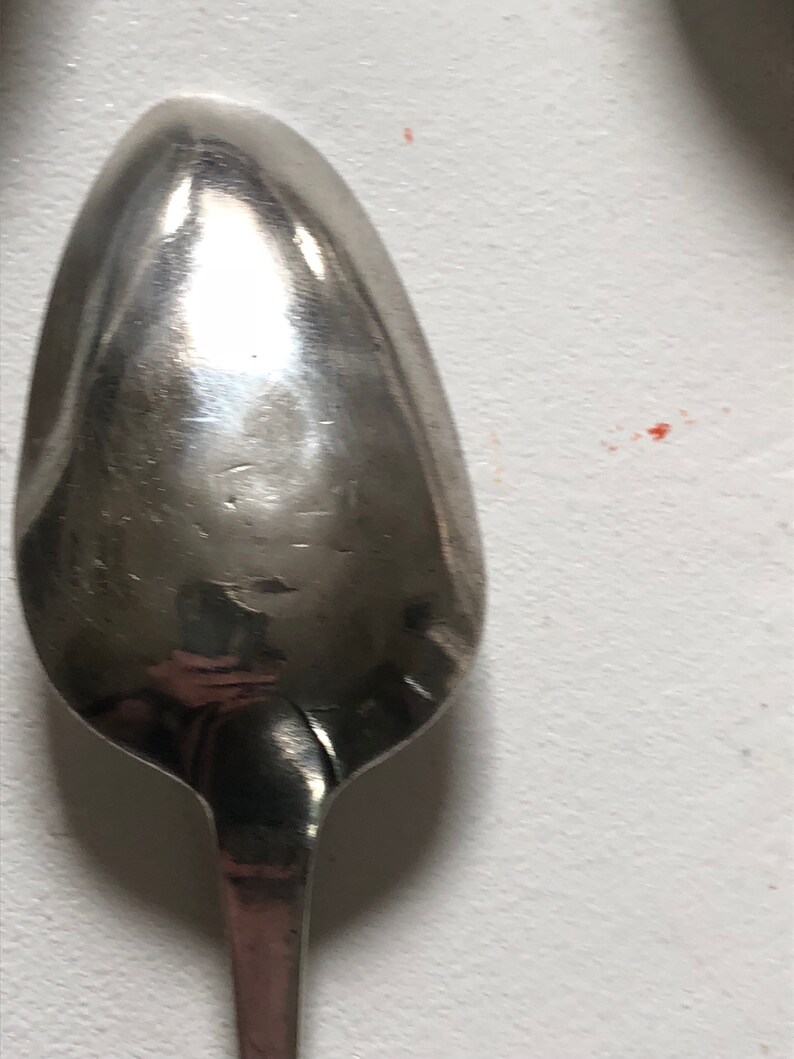 Puede incluir: Una cuchara de plata con un cuenco redondeado de forma ovalada. La cuchara est&aacute; pulida y refleja la luz.