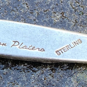 Op de afbeelding: Close-up van een zilveren metalen voorwerp met de inscriptie "Don Platero Sterling" gegraveerd op het oppervlak.