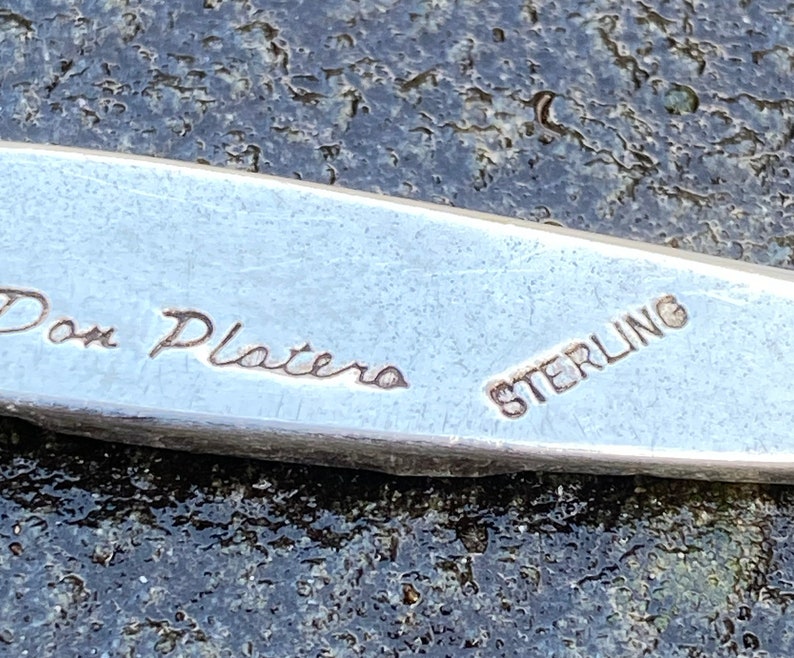 Op de afbeelding: Close-up van een zilveren metalen voorwerp met de inscriptie "Don Platero Sterling" gegraveerd op het oppervlak.