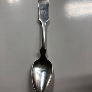 May include: A silver spoon with a rounded bowl and a long, slender handle. The handle is engraved with the word "Wife".