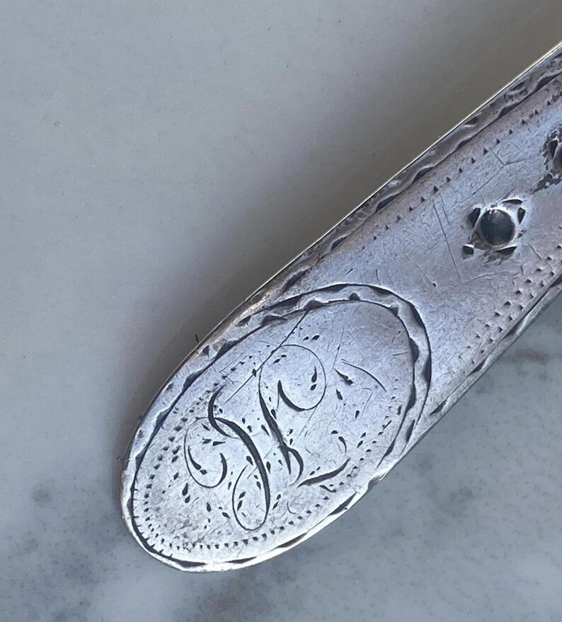 May include: Close-up of a silver spoon handle with an engraved oval containing the letter "F".
