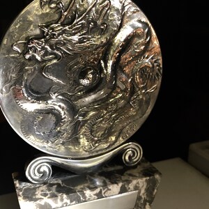 May include: A silver trophy with a dragon design on a round base. The base is attached to a marble base with a silver plaque.