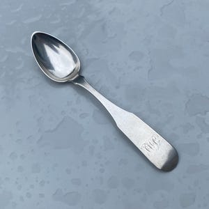 May include: A silver teaspoon with an oval bowl and a long, slender handle. The handle is engraved with the initials "A.W.B."