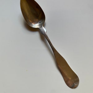 May include: A silver spoon with a rounded bowl and a long, slender handle. The handle is engraved with the word "Alice".
