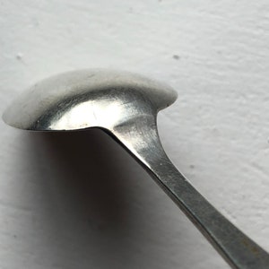 Puede incluir: Una cucharita de plata con un cuenco redondeado y un mango largo y delgado.