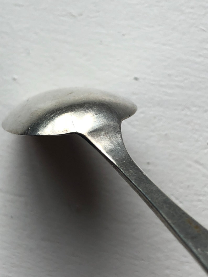 Puede incluir: Una cucharita de plata con un cuenco redondeado y un mango largo y delgado.