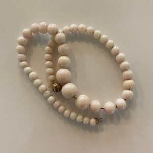 May include: A white pearl necklace with a gold clasp. The pearls are round and have a slight pink hue.