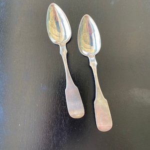 May include: Two silver spoons with ornate handles. The spoons have a rounded bowl shape and are polished to a shine.