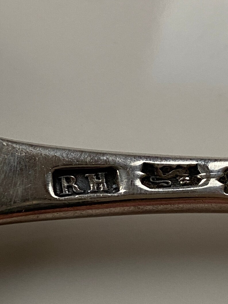 K&ouml;nnte beinhalten: Nahaufnahme eines silbernen L&ouml;ffels mit den eingravierten Initialen "R.H.".