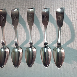 May include: Six silver teaspoons with ornate handles. Each spoon has an inscription on the handle.