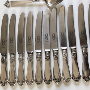 Puede incluir: Un juego de 13 cuchillos de cena de plata con mangos ornamentados. Los cuchillos tienen un acabado pulido y presentan un dise&ntilde;o decorativo en los mangos.