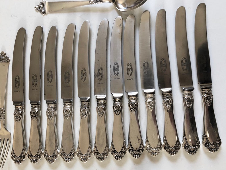 Puede incluir: Un juego de 13 cuchillos de cena de plata con mangos ornamentados. Los cuchillos tienen un acabado pulido y presentan un dise&ntilde;o decorativo en los mangos.