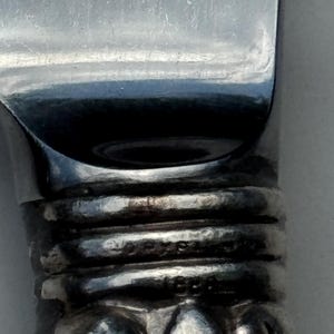 May include: Close-up of a silver knife with a reflective blade. The handle has textured rings and a decorative base. The word "STERLING" is visible on the handle.