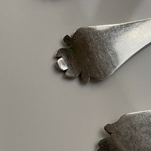 May include: Close-up of a silver spoon with a decorative, ornate handle. The handle is shaped like a foot with a detailed design.