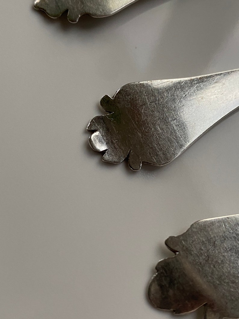 May include: Close-up of a silver spoon with a decorative, ornate handle. The handle is shaped like a foot with a detailed design.