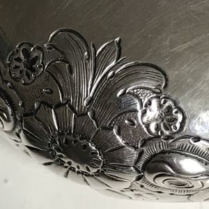 以下が含まれることがあります： 縁に複雑な花柄が彫刻された銀製のボウルをクローズアップした写真です。