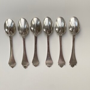 May include: Six silver teaspoons with ornate handles. The spoons are arranged in a row, with the handles facing the viewer.