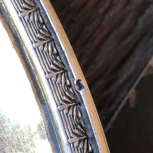 Puede incluir: Primer plano del borde de una bandeja de servir de plata con un borde decorativo de dise&ntilde;os de hojas repetidos.