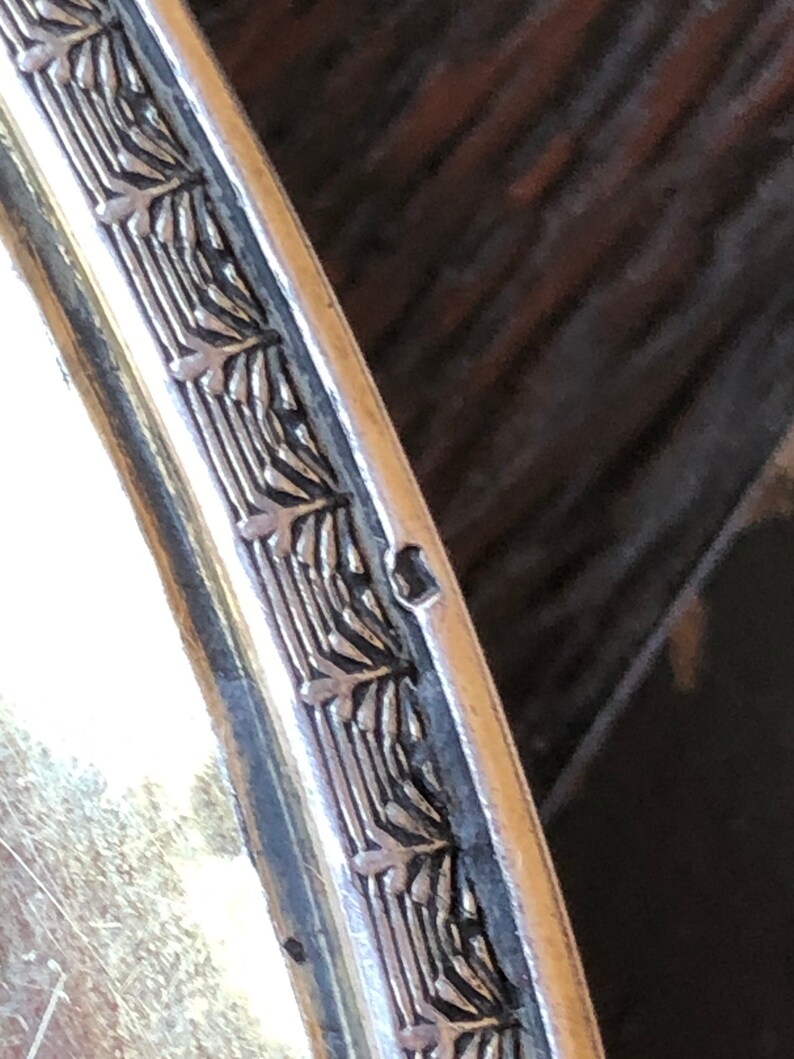 Puede incluir: Primer plano del borde de una bandeja de servir de plata con un borde decorativo de dise&ntilde;os de hojas repetidos.