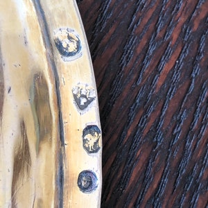 Puede incluir: Primer plano de una bandeja de plata con cuatro marcas de contraste. Las marcas de contraste son en forma de c&iacute;rculo, cuadrado, rombo y rect&aacute;ngulo. La bandeja est&aacute; hecha de un metal brillante y tiene una superficie lisa.