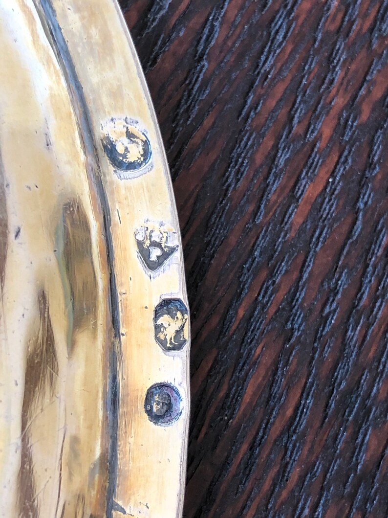 Puede incluir: Primer plano de una bandeja de plata con cuatro marcas de contraste. Las marcas de contraste son en forma de c&iacute;rculo, cuadrado, rombo y rect&aacute;ngulo. La bandeja est&aacute; hecha de un metal brillante y tiene una superficie lisa.