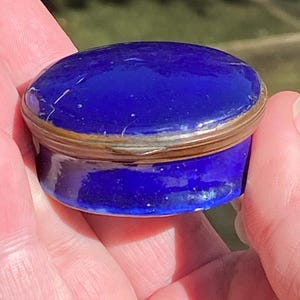 May include: A small, round, blue enamel trinket box with a silver lid.