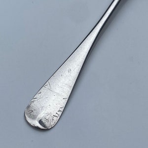 K&ouml;nnte beinhalten: Ein silberner Teel&ouml;ffel mit einer abgerundeten Schale und einem langen, schlanken Stiel. Der Stiel ist mit einer Reihe von Kratzern und Linien versehen.