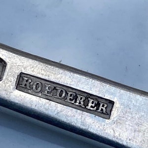 May include: Close-up of a silver metal object with the word "ROEDERER" engraved on it.