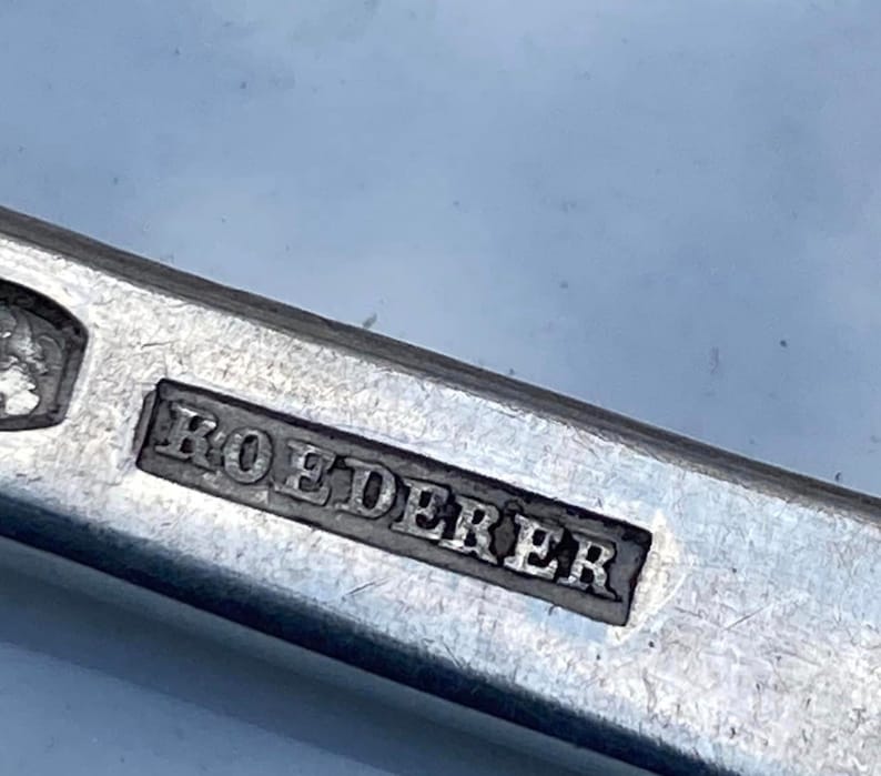 May include: Close-up of a silver metal object with the word "ROEDERER" engraved on it.