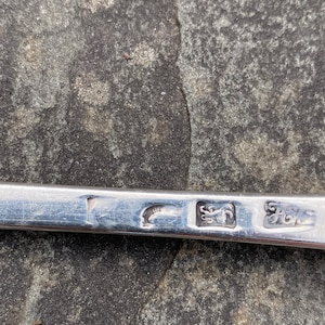 May include: Close-up of a silver spoon with hallmarks. The hallmarks include a crescent moon, a lion, and the letter "G".