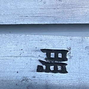 K&ouml;nnte beinhalten: Nahaufnahme einer silbernen Metalloberfl&auml;che mit einem schwarzen Kanji-Zeichen, das darauf eingepr&auml;gt ist. Das Zeichen ist eine stilisierte Darstellung eines dreist&ouml;ckigen Geb&auml;udes.