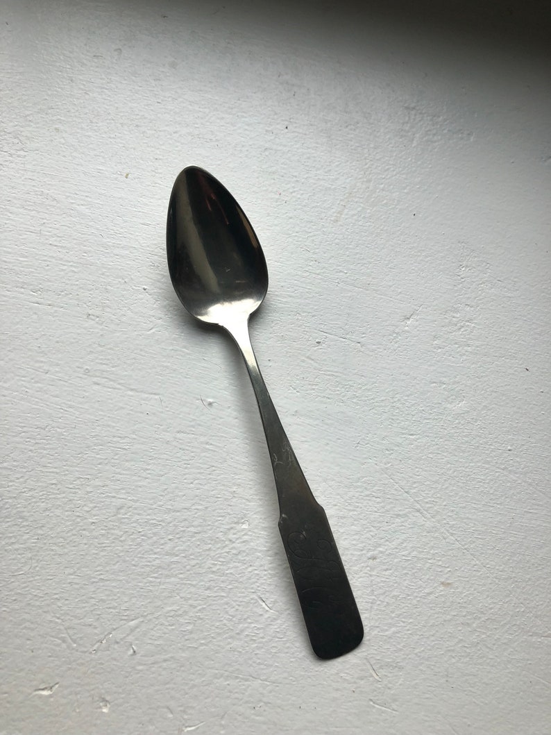 Puede incluir: Una cuchara de plata con un cuenco redondeado y un mango largo y estrecho. El mango tiene un dise&ntilde;o decorativo.