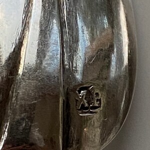 May include: Close-up of a silver spoon with a hallmark that reads "XE".