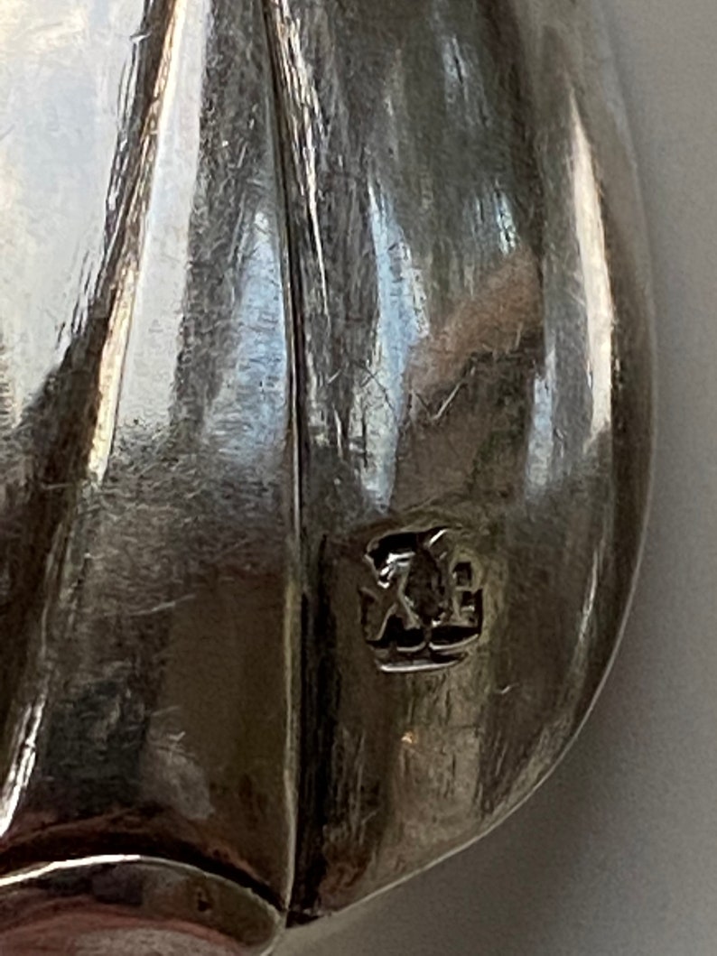 May include: Close-up of a silver spoon with a hallmark that reads "XE".