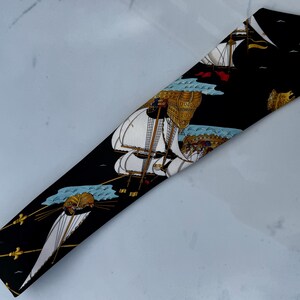 Puede incluir: Corbata negra con un patr&oacute;n repetido de veleros con velas blancas y detalles dorados. Los barcos navegan sobre aguas azules sobre un fondo negro. La corbata tiene una forma cl&aacute;sica y est&aacute; hecha de una tela suave.