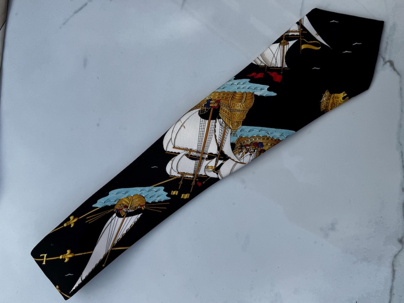 Puede incluir: Corbata negra con un patr&oacute;n repetido de veleros con velas blancas y detalles dorados. Los barcos navegan sobre aguas azules sobre un fondo negro. La corbata tiene una forma cl&aacute;sica y est&aacute; hecha de una tela suave.