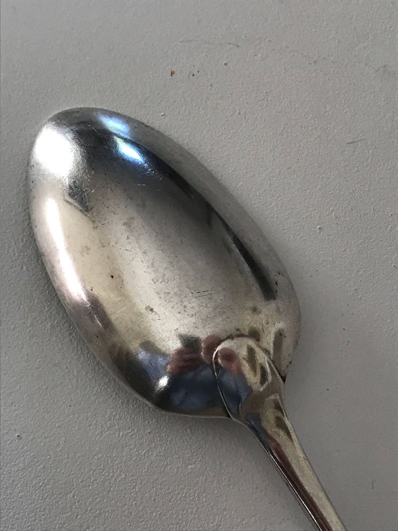 Może przedstawiać: Zbliżenie srebrnej łyżki z zaokrągloną miseczką i długim, smukłym trzonkiem. Łyżka odbija otoczenie, ukazując błyszczącą, wypolerowaną powierzchnię. Łyżka jest prawdopodobnie używana do jedzenia lub serwowania potraw.