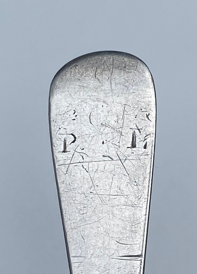 K&ouml;nnte beinhalten: Nahaufnahme der Oberseite eines silbernen L&ouml;ffels mit der Inschrift "I.M." auf der R&uuml;ckseite.