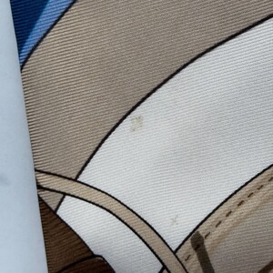 Puede incluir: Pa&ntilde;uelo de seda con un dise&ntilde;o geom&eacute;trico en tonos azul, beige y blanco. El pa&ntilde;uelo presenta l&iacute;neas curvas y un patr&oacute;n que recuerda elementos ecuestres.