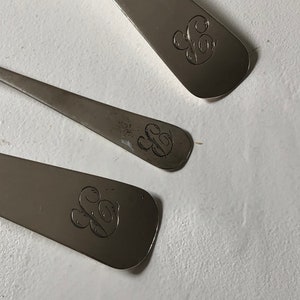 Puede incluir: Tres cucharas de plata con un dise&ntilde;o grabado de una letra 'S' estilizada en la parte posterior de cada cuchara.