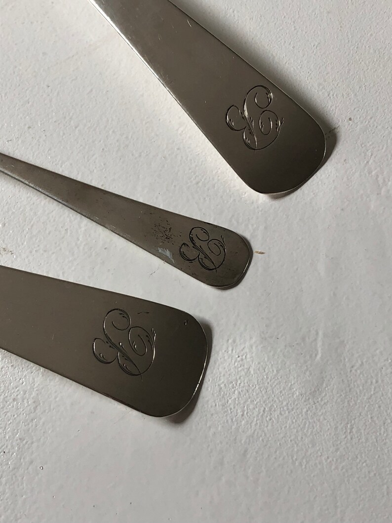 Puede incluir: Tres cucharas de plata con un dise&ntilde;o grabado de una letra 'S' estilizada en la parte posterior de cada cuchara.